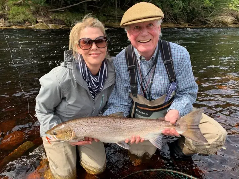 A guest and a guide kneel in the River Findhorn holding a salmon between them
