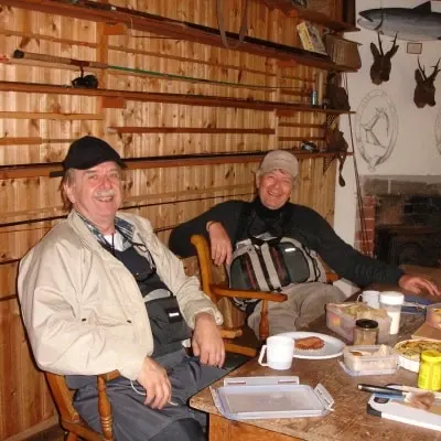 Two anglers smiling over a picnic lunch in a wood panelled fishing hut on the River Findhorn
