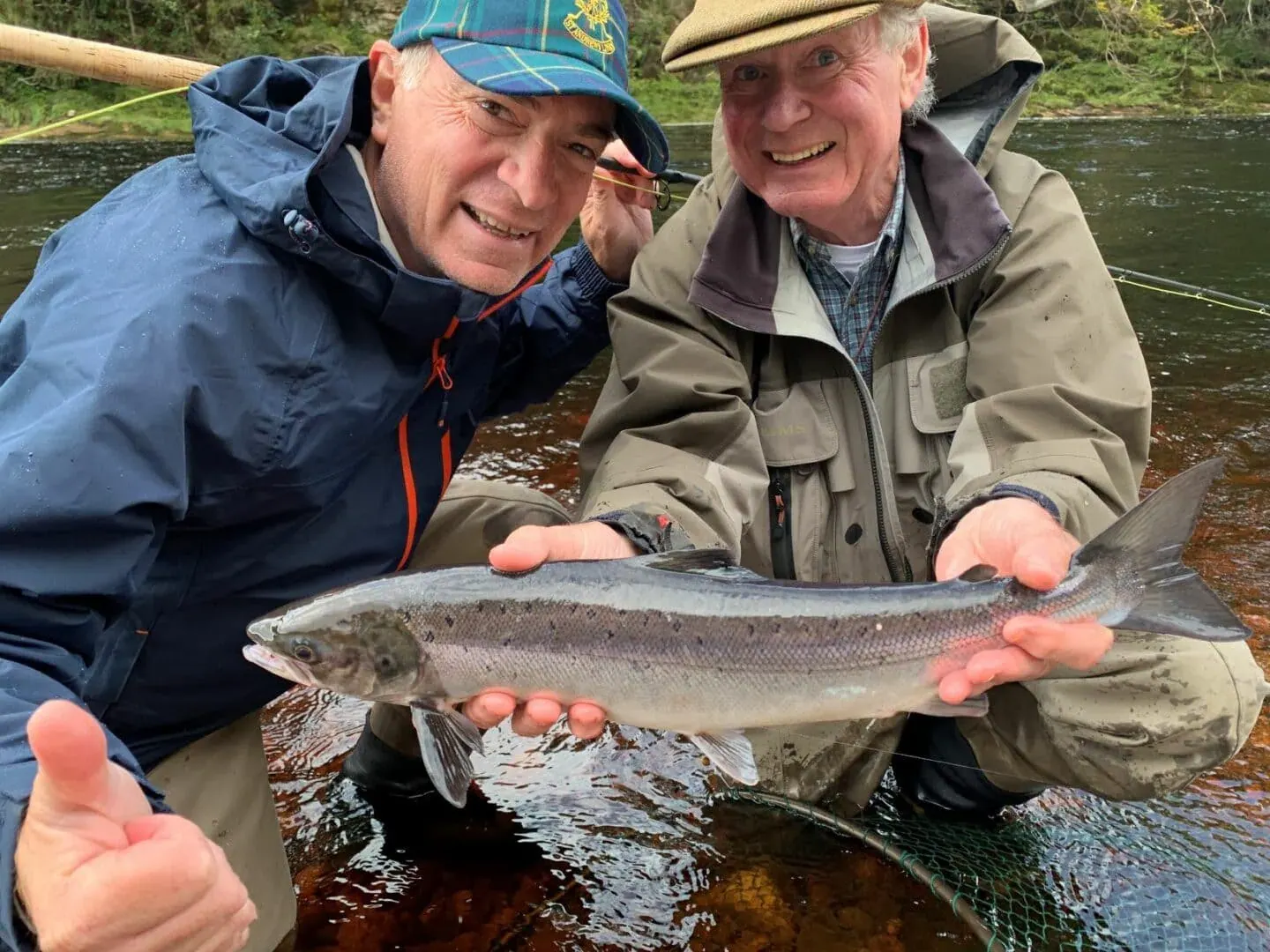Two anglers kneeling in a river smiling while holding a freshly caught salmon