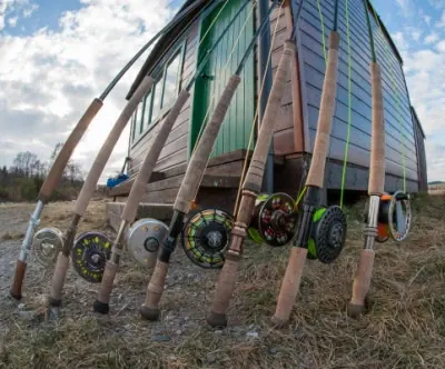 Spey rods and reels with coloured fly lines lean against a wooden fishing hut