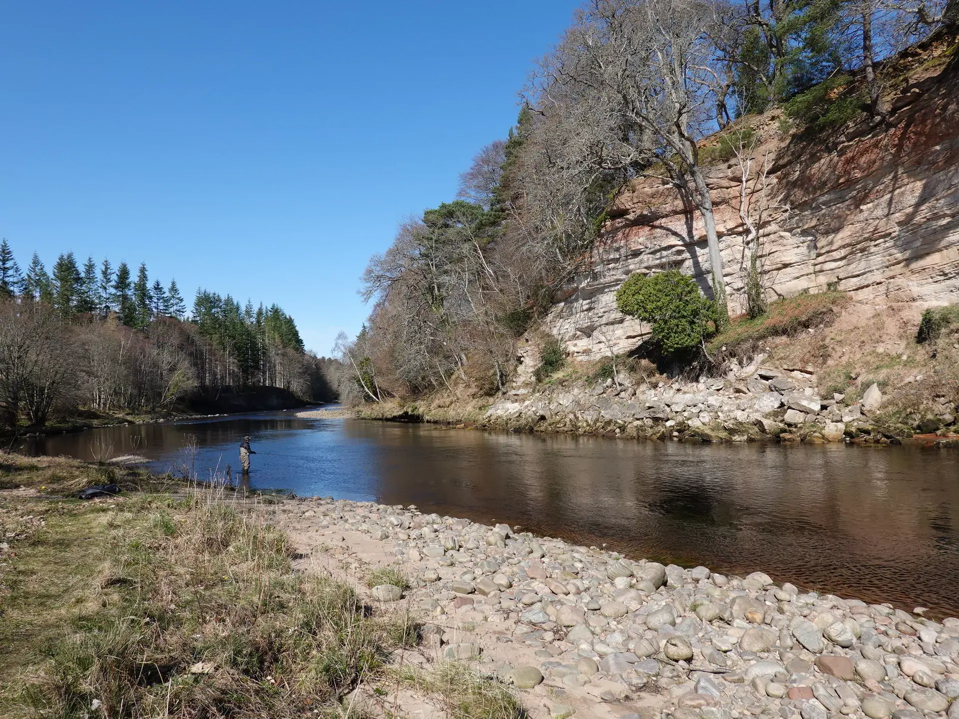An angler Spey casting below sandstone cliffs on the Findhorn's Meads of St John beat