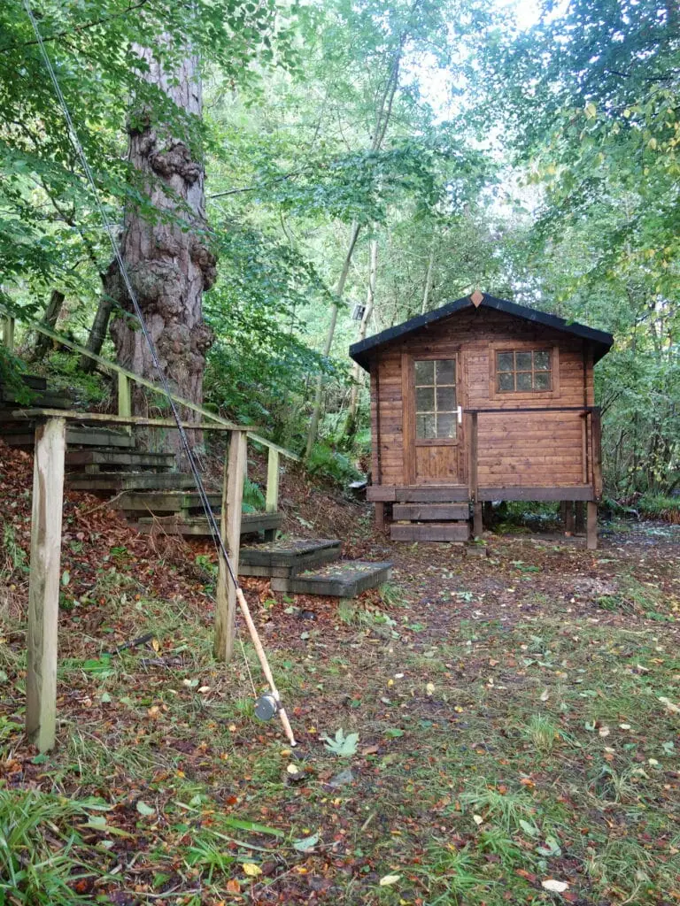 A wooden fishing hut and steps in woodland above the Tweed, with a rod resting against the railing