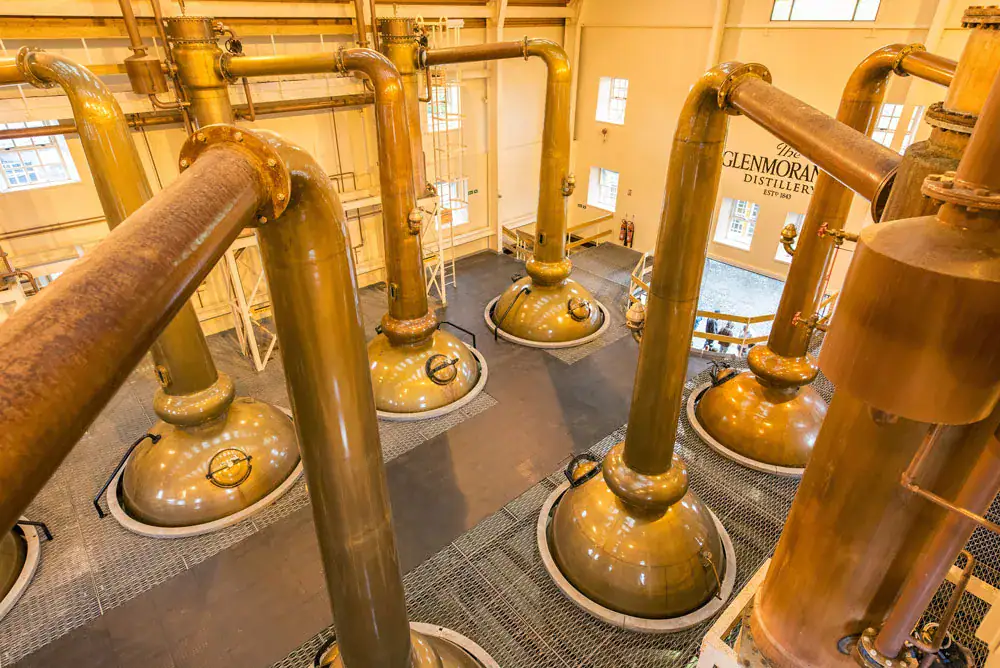 Tall copper pot stills inside the Glenmorangie Distillery still house, viewed from above