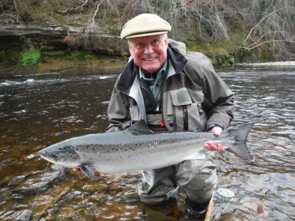 A smiling angler kneels in the River Findhorn holding a spring salmon near Soldier's Hole pool