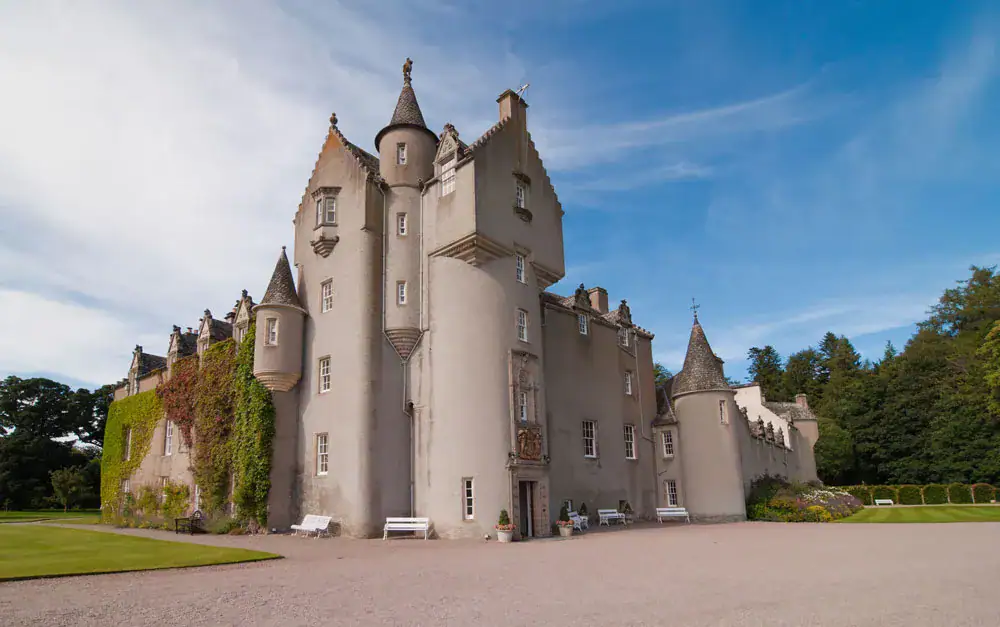 Ballindalloch Castle's turreted facade with ivy covered walls and manicured lawns under a blue sky
