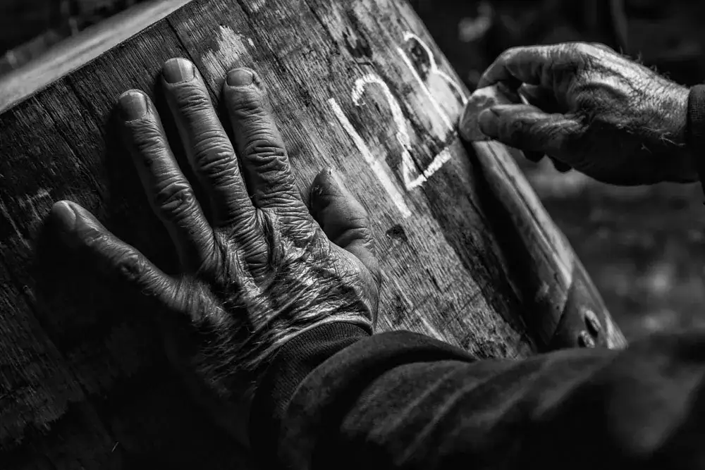 Black and white close up of a worker's hands chalking a number on a whisky cask