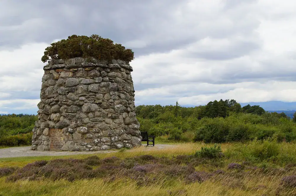 Stone cairn memorial at Culloden battlefield amid heather moorland under a cloudy sky
