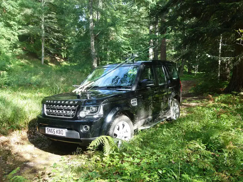 Black Land Rover Discovery parked on a forest track in Darnaway Forest on a sunny summer day