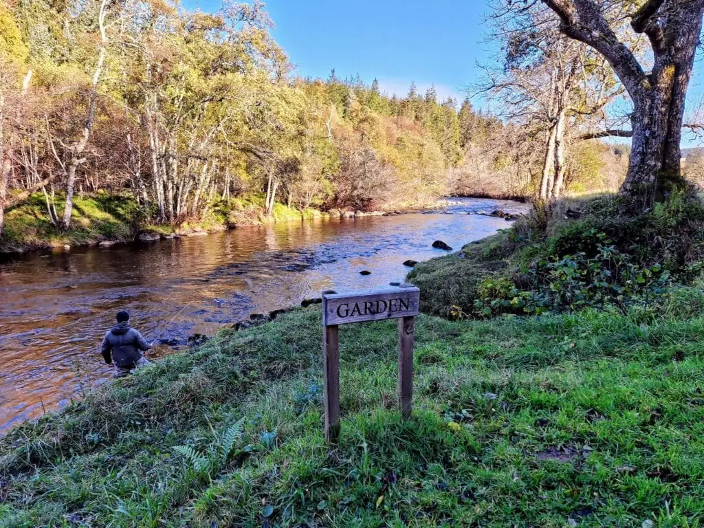 An angler wading the River Alness beside the Garden pool sign on an autumn day
